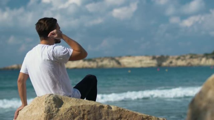 年轻英俊的男人坐在神奇的大海附近的石头上