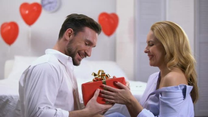 迷人的年轻女性送红色礼盒给惊讶的男友，周年纪念