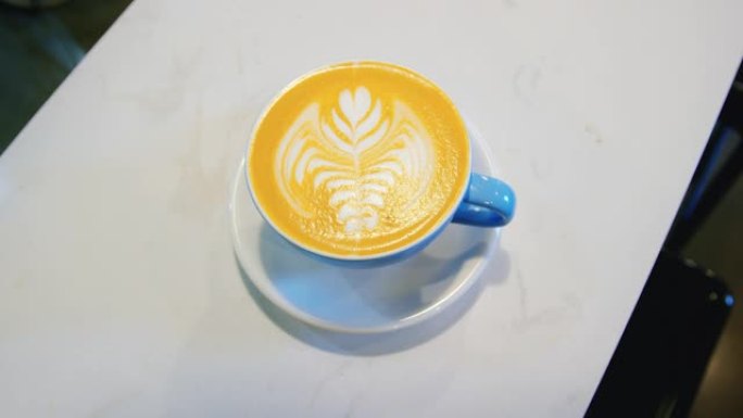 咖啡师在咖啡店的柜台上放了一个小碟和蓝色咖啡杯，上面装有拿铁咖啡