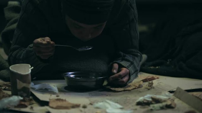 手抖的无家可归者贪婪地吃汤，肮脏的住所，饥荒