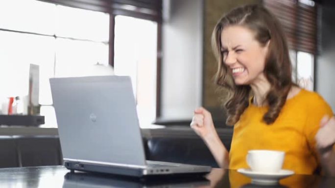 兴奋的女人在咖啡馆使用笔记本电脑，赢得在线彩票，胜利之舞