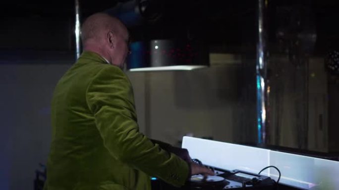 开朗的白人老人在控制器上混合音乐并在夜总会向游客挥手的侧视图。高级男DJ在迪斯科娱乐人们。生活方式，