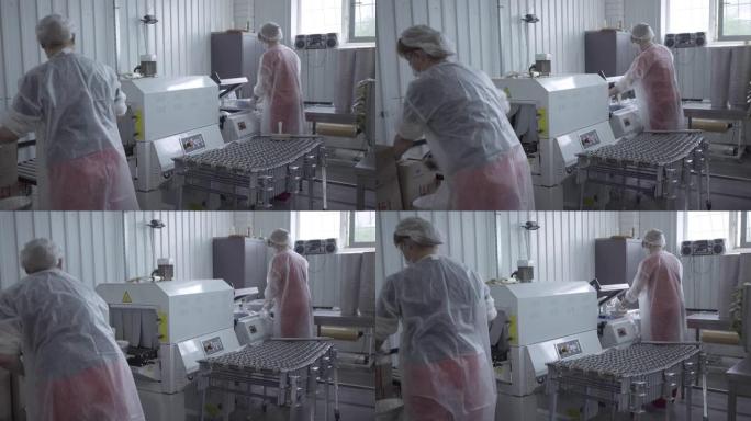 两名妇女在工厂吸尘机工作的后侧视图。成年高加索员工包装食品包装在检疫制造厂销售。生活方式，生产，制造