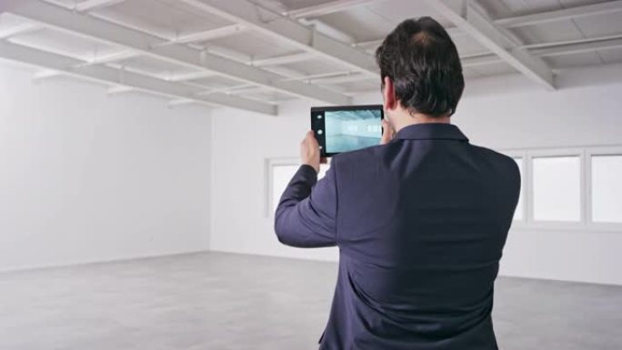 男性投资者使用他的数字平板电脑为空荡荡的商业大楼中的办公空间拍照