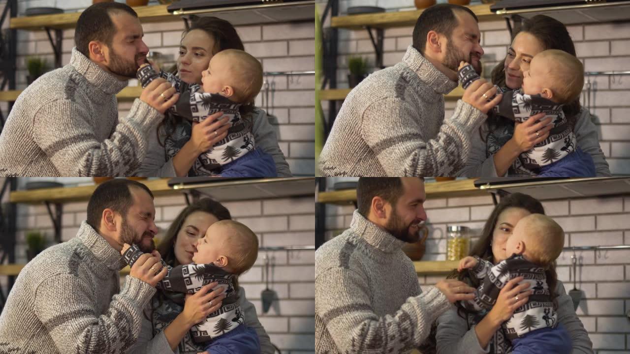 微笑的父亲穿着温暖的毛衣，与在母亲怀抱中的小儿子在厨房里玩耍。