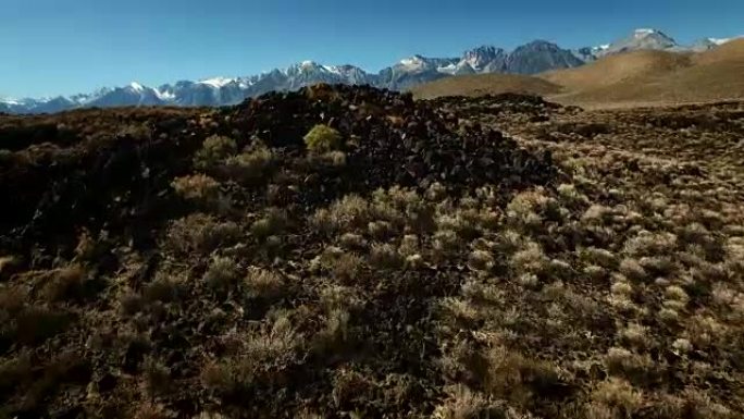 无人机拍摄开始于岩石和干燥的土地上，在晨曦中露出美丽的雪顶山脉。