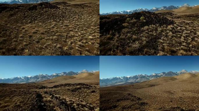 无人机拍摄开始于岩石和干燥的土地上，在晨曦中露出美丽的雪顶山脉。