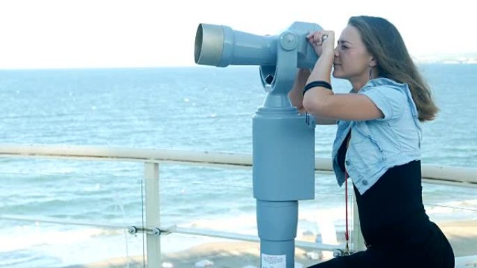 可爱的女孩通过硬币操作的小望远镜或公共望远镜看大海