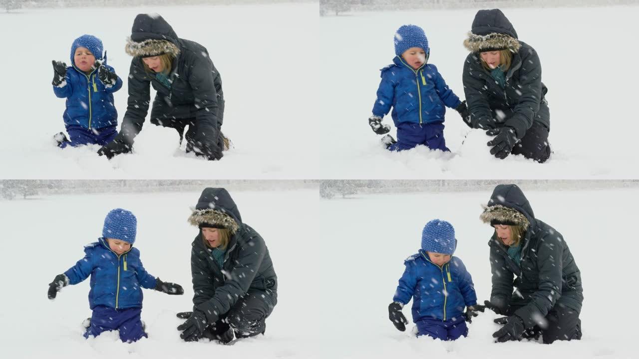 三岁的高加索男孩和他三十多岁的高加索母亲 (都穿着冬装) 在下雪的阴天一起堆雪人