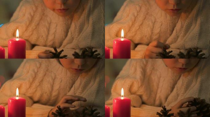女孩看着松果，蜡烛燃烧在附近，圣诞工艺品特写