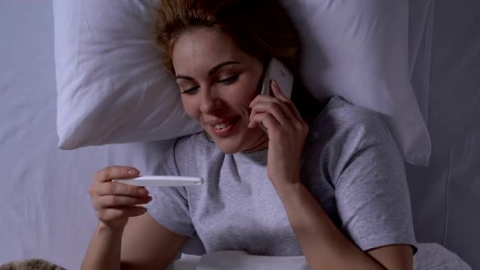 微笑的女人在床上拿着怀孕测试和通话电话，阳性结果