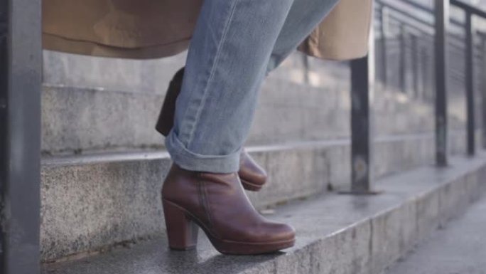 穿着牛仔裤和棕色靴子的女性高加索腿走下楼梯的特写镜头。生活方式，匆忙，商人。