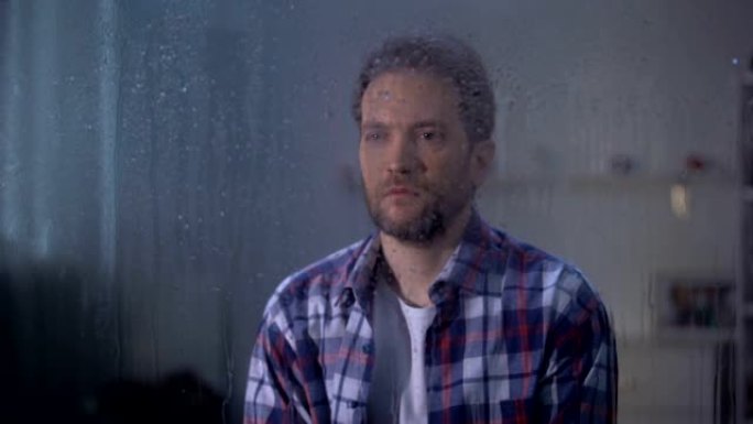 孤独悲伤的中年男子透过阴雨的窗户，恶劣的天气条件