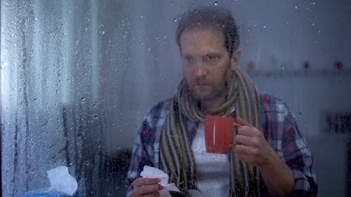 生病的男人在雨天打喷嚏并在家里喝热茶，流感病毒