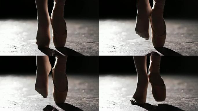 在工作室的黑色背景上，女性双腿在聚光灯下摆姿势。一只脚在足尖，另一只脚在脚趾上没有鞋。