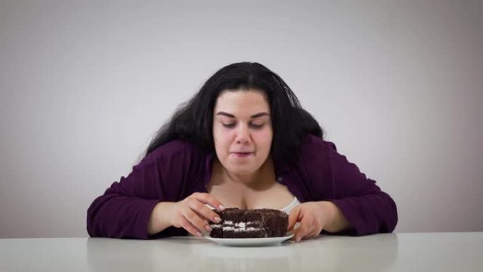 黑发胖女孩环顾四周，咬一块巧克力蛋糕的肖像。有超重问题的白人妇女吃甜食。自我控制，肥胖，不健康的生活