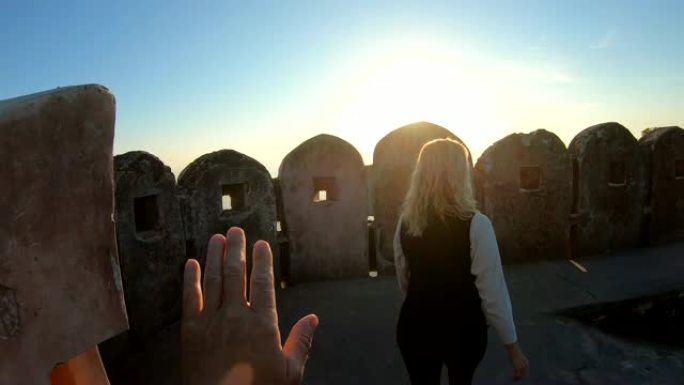 女人在日出时沿着古老的堡垒墙行走