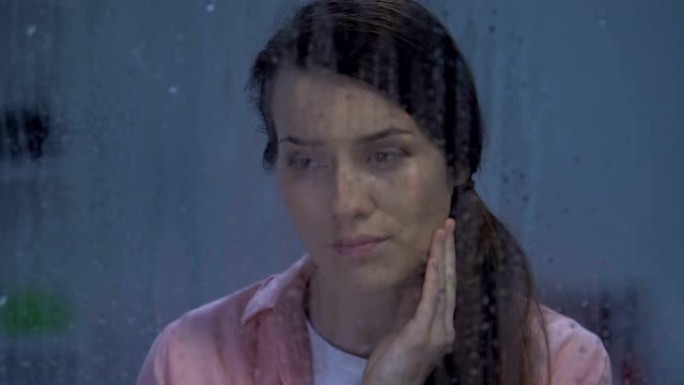 离婚后沮丧的女士在下雨的窗户后面哭泣，遭受沮丧