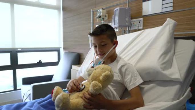 可爱的住院小男孩用听诊器检查他的泰迪熊的心脏