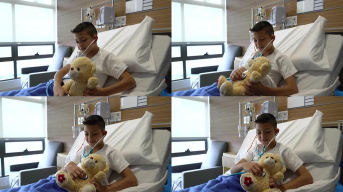 可爱的住院小男孩用听诊器检查他的泰迪熊的心脏