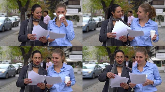 女性商业伙伴在享受外卖咖啡的同时非常愉快地在外面检查一些文件