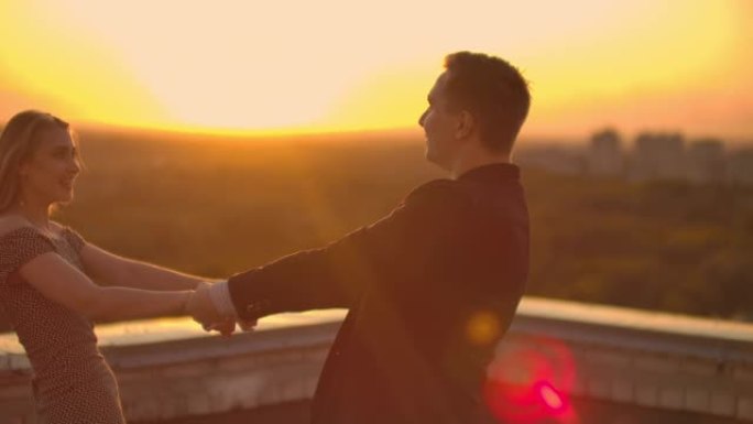 一个恋爱中的男人和一个女人在日落时站在建筑物的屋顶上跳舞，互相看着对方