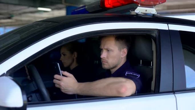 男人和女人警察使用坐在巡逻车中的智能手机，监视城市应用程序