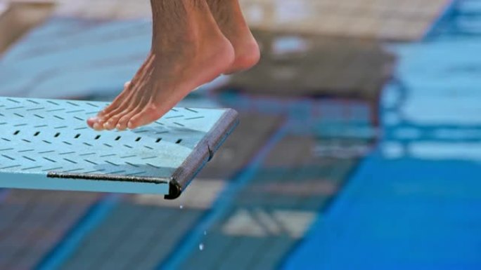 一名男性潜水员的SLO MO脚站在跳水板的边缘跳入游泳池