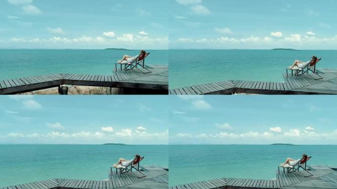女人在沙滩上舒适的椅子上喝椰子水