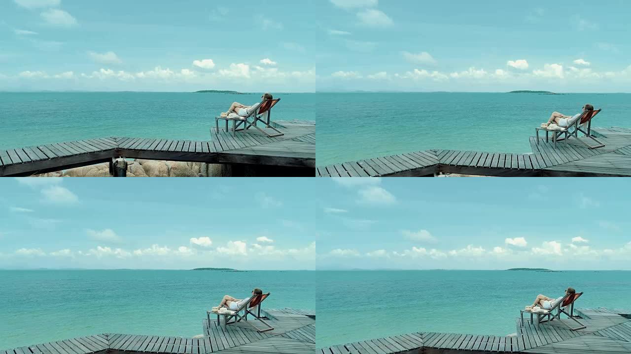 女人在沙滩上舒适的椅子上喝椰子水