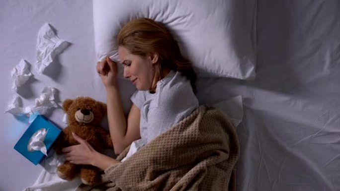 沮丧的女人在床上哭泣，拥抱泰迪熊，流产