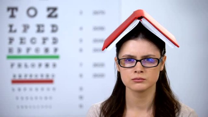 头上拿着书的女士看着相机，过度劳累的学生准备考试