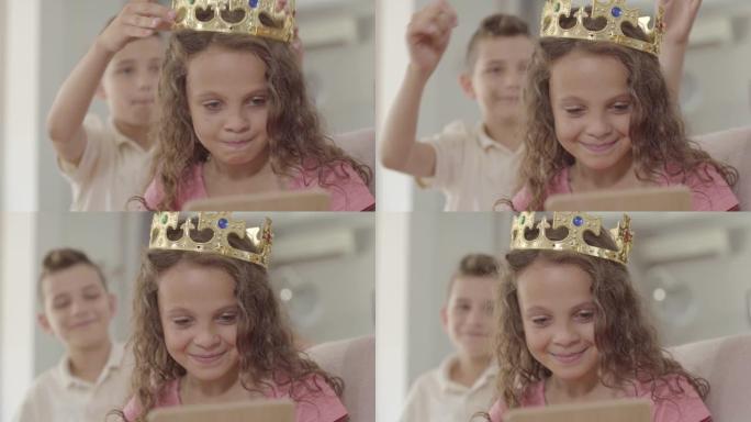 可爱的男孩把皇冠戴在看着镜子的可爱的卷发女孩的头上。