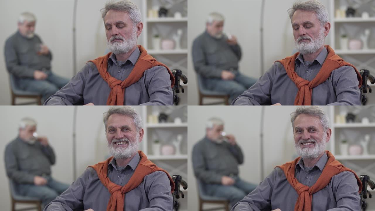 开朗的白人男子的肖像突然看着相机并微笑。积极的老人坐在养老院的轮椅上，背景模糊。