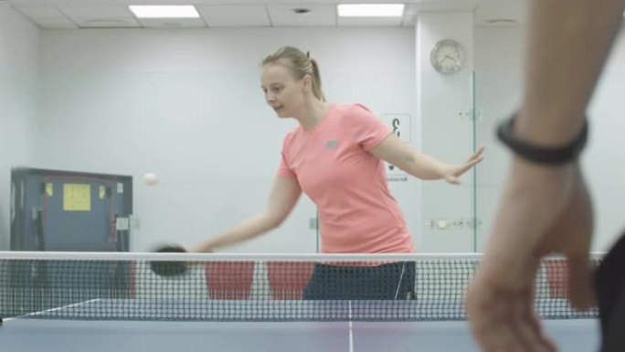 正面金发女运动员在乒乓球比赛中获胜的肖像。开朗微笑的年轻白人女子打乒乓球，在健身房做胜利手势。