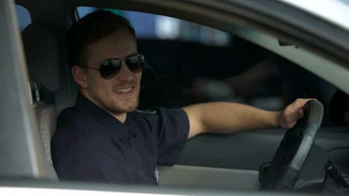 开朗的男警察戴着太阳镜坐在巡逻车里，对着镜头微笑