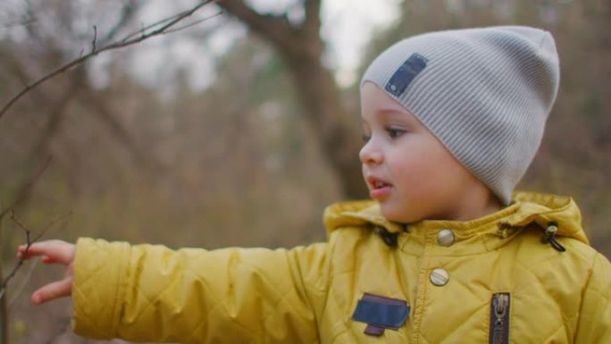 快乐的笑声和微笑的男孩2岁在森林里看着镜头。迷人可爱的大睫毛男孩。一个穿黄色夹克和帽子的男孩