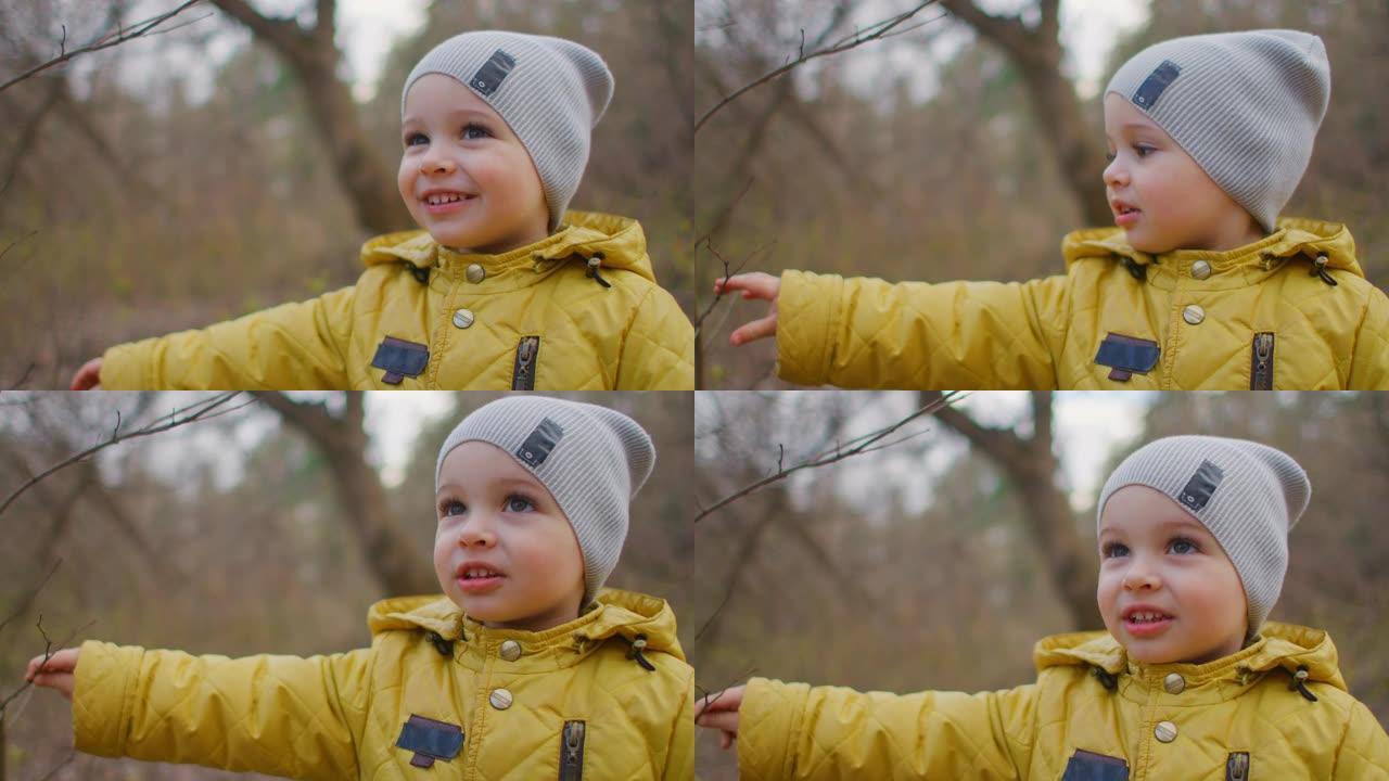 快乐的笑声和微笑的男孩2岁在森林里看着镜头。迷人可爱的大睫毛男孩。一个穿黄色夹克和帽子的男孩