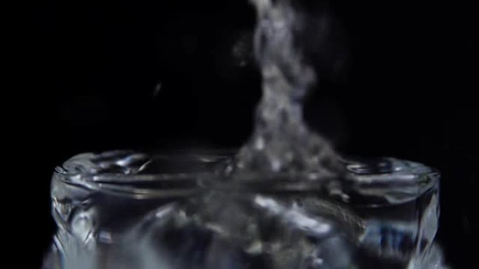 冰块落在装有水的玻璃杯中。黑色背景上的慢动作