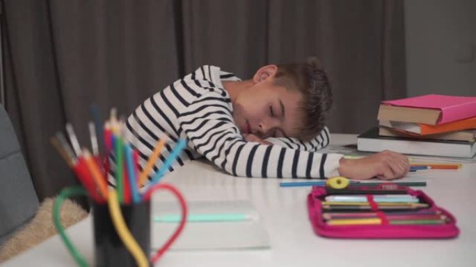 一个白人小男孩睡在桌子上的特写脸。小学生在家做作业后累了。可爱的孩子穿着条纹夹克学习后筋疲力尽。