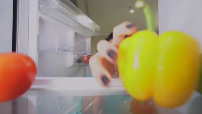 有吸引力的混血妇女从冰箱中摄取新鲜辣椒，健康营养
