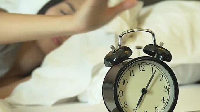4K: 睡在床上的亚洲女人用手关闭闹钟，用闹钟特写。