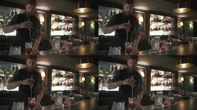 专业的大胡子调酒师用长金属棒在玻璃杯中混合朗姆酒和冰。