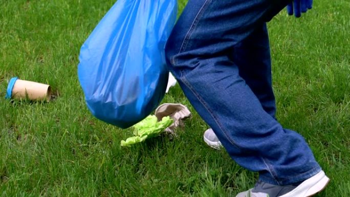 不负责任的男子在草坪上扔纸杯后，男性志愿者在捡垃圾