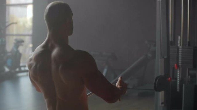 一名男子坐在模拟器中，在健身房大窗户的背景下，对背部肌肉进行锻炼，将体重拉到腹部。有实力的男运动员划