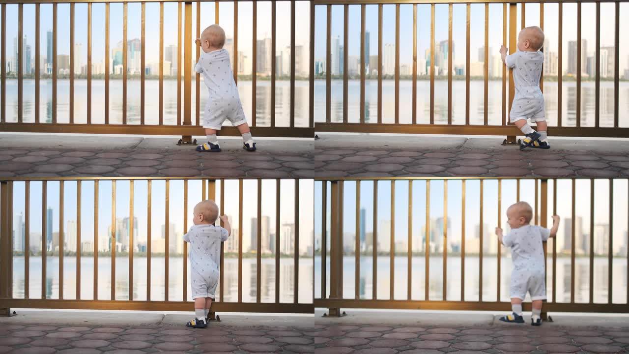 在阿联酋夏天，在篱笆附近跳舞的欢快的欧洲男孩一直在栏杆上跳舞，站着跳舞，看着长廊的景色