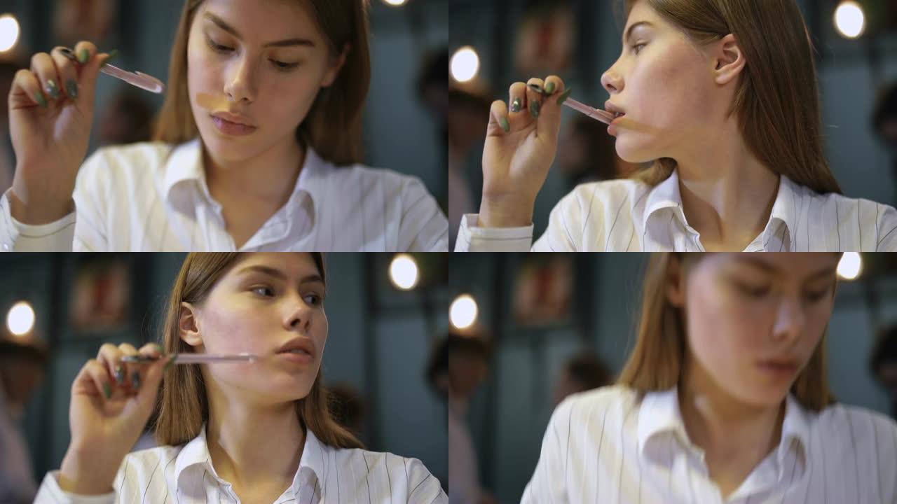 一个穿着白衬衫的年轻女孩的肖像坐在咖啡馆里，拿着笔靠近嘴唇。