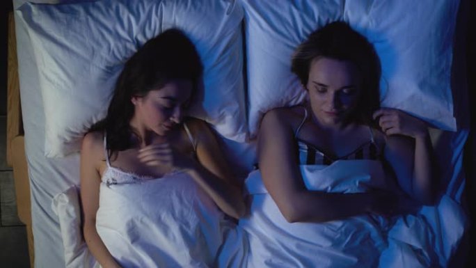 两名年轻女子晚上睡在舒适的床上，聚会后休息