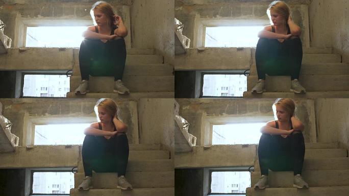 年轻不快乐的女孩坐在一栋废弃建筑的楼梯上