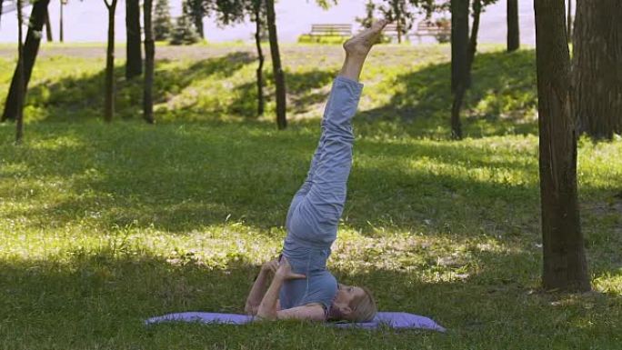 高级健身女性在公园垫子上做瑜伽，肩立体态，慢动作